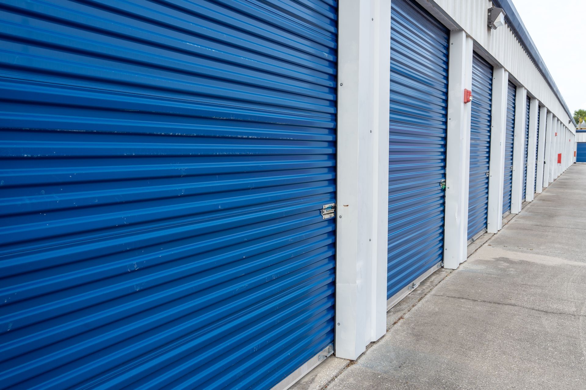 Row of blue storage unit doors along a concrete corridor at a self-storage facility