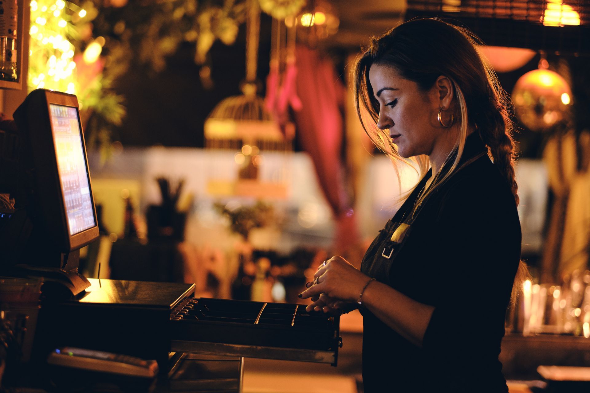 Bartender working behind a glowing bar at night, lit by warm amber lights.