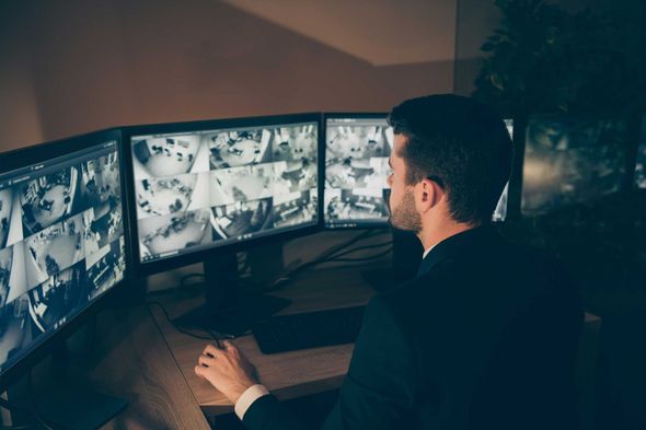 Person monitoring multiple security camera feeds on several screens in a dimly lit control room