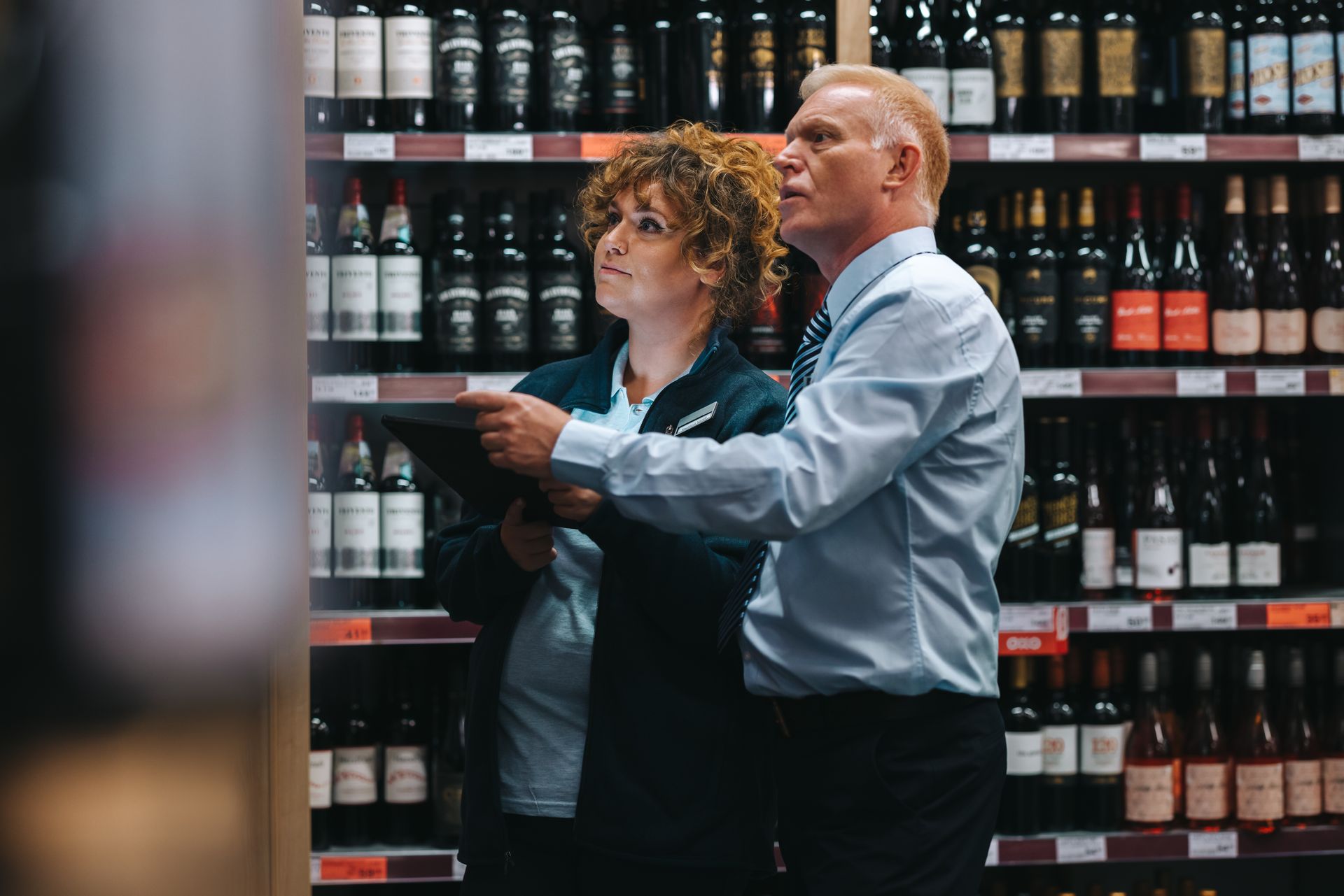 Two shoppers examining wine bottles on shelves in a store