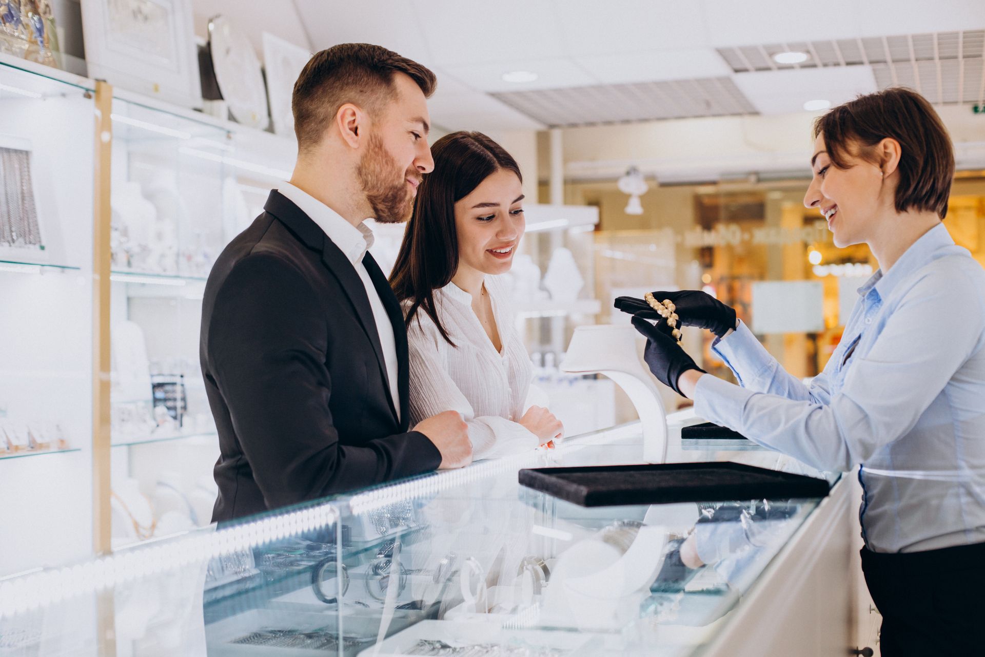 Customer and salesperson talking across a jewelry store counter, with watches and display cases visible.