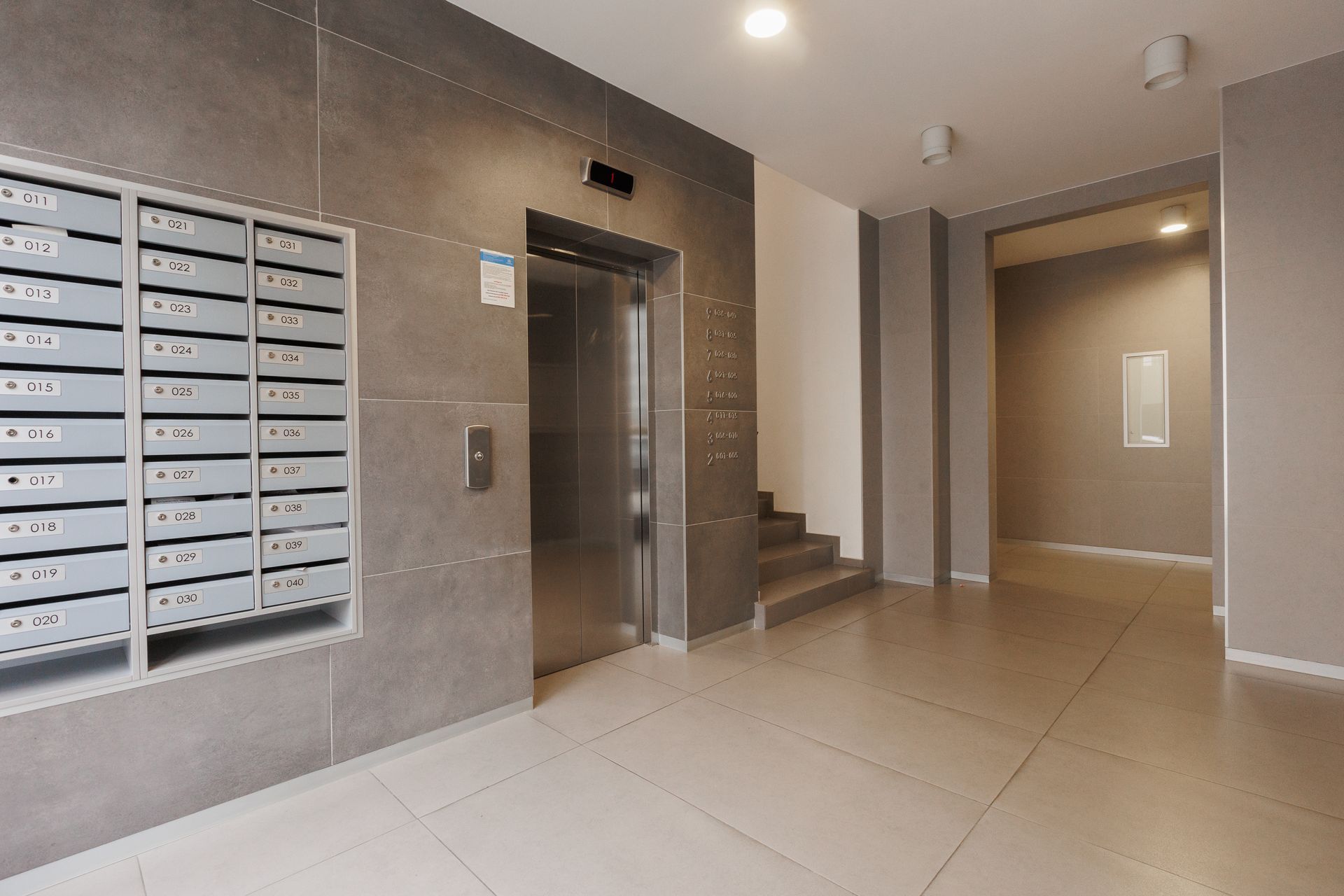 Apartment lobby with mailboxes, elevator, and stairwell in a beige hallway