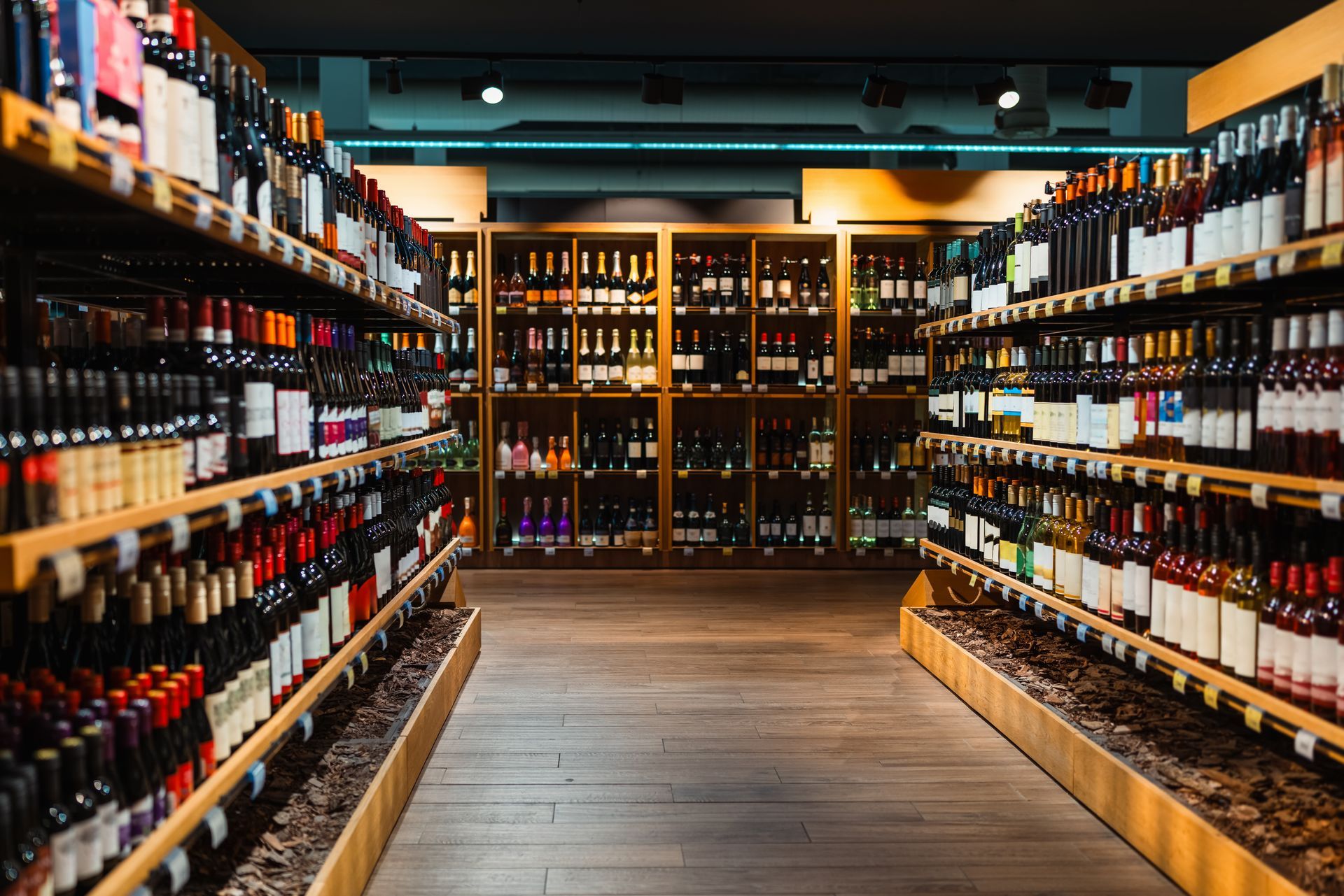 Wine bottles lining shelves in a warmly lit store aisle, with rows on both sides and a back display.