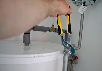 A person is fixing a water heater with a wrench.
