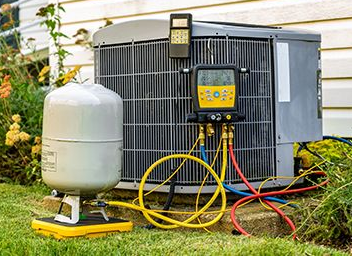 Outdoor HVAC unit beside house with yellow, red, and blue service hoses and a white tank on the lawn