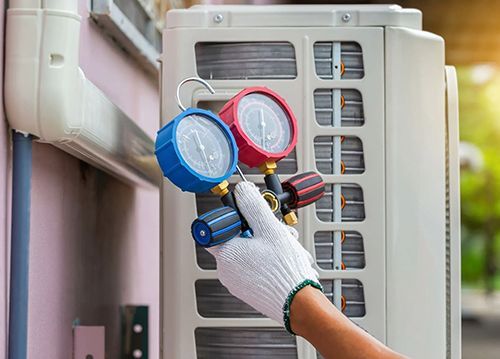 A person is holding two gauges in front of an air conditioner.