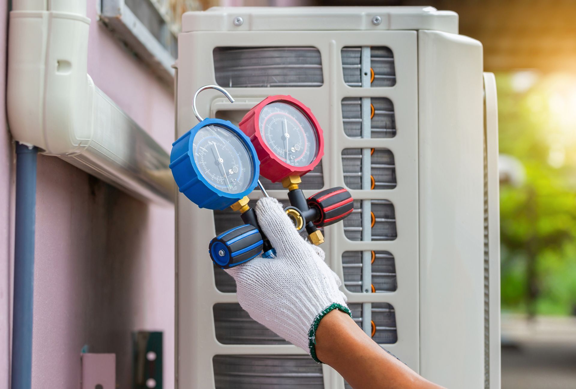 A person is holding two gauges in front of an air conditioner.