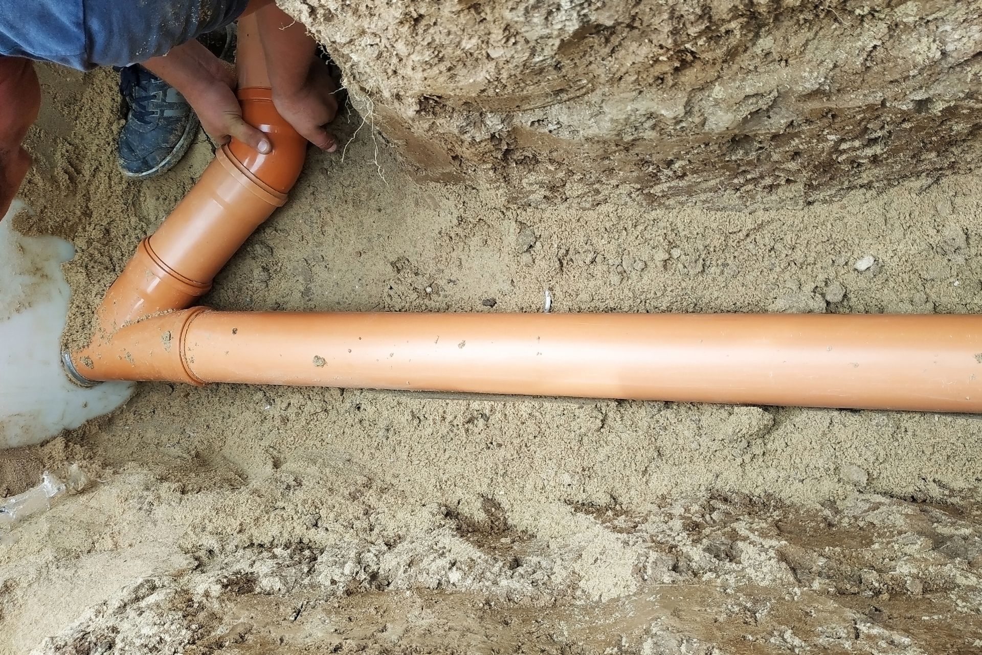 A person is working on a pipe in the dirt.