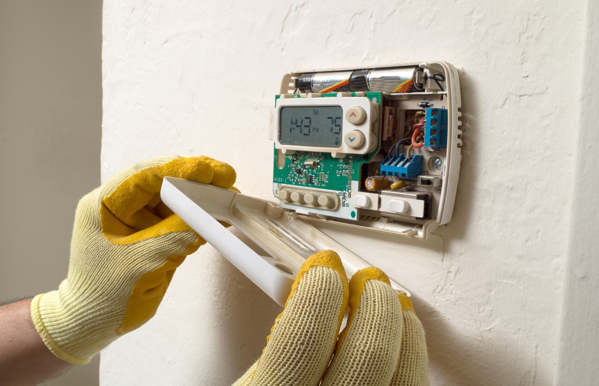 A person wearing yellow gloves is fixing a thermostat on a wall.