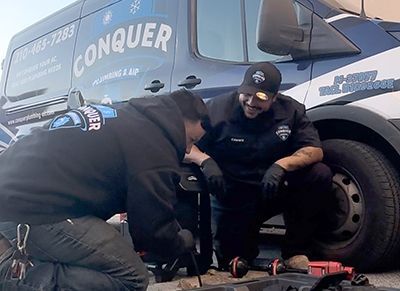 two men are working on a vehicle in front of a conquer van .