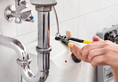 Plumber using wrench on a water heater, chrome pipes and fittings, indoors.