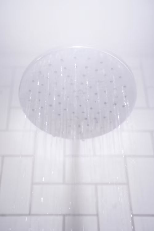 Round showerhead spraying water in a tiled shower.