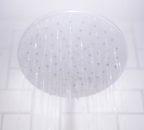 Round silver showerhead spraying water in a tiled bathroom ceiling view
