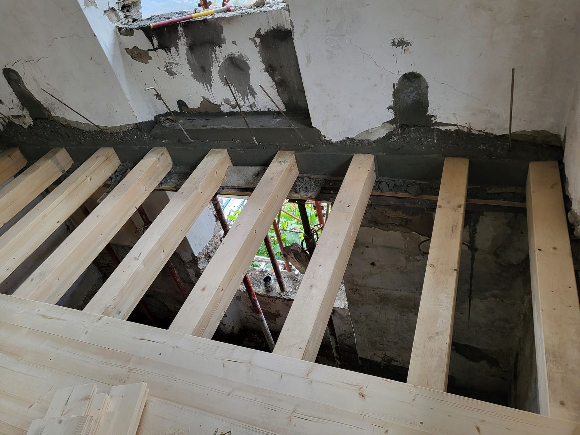 Travi di legno che sostengono una struttura in cemento durante la costruzione, con vista attraverso un'apertura sottostante.