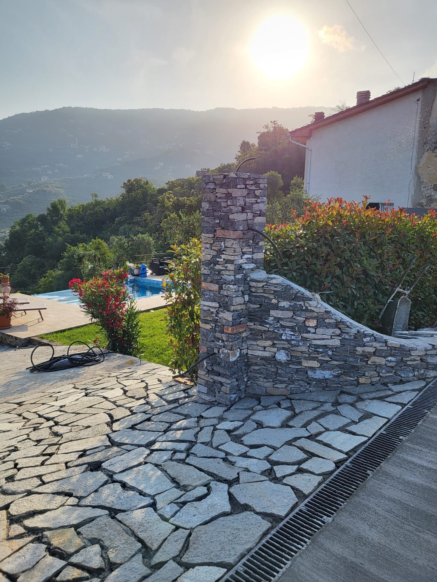 Patio in pietra e muro con vista su una collina con piscina al tramonto.