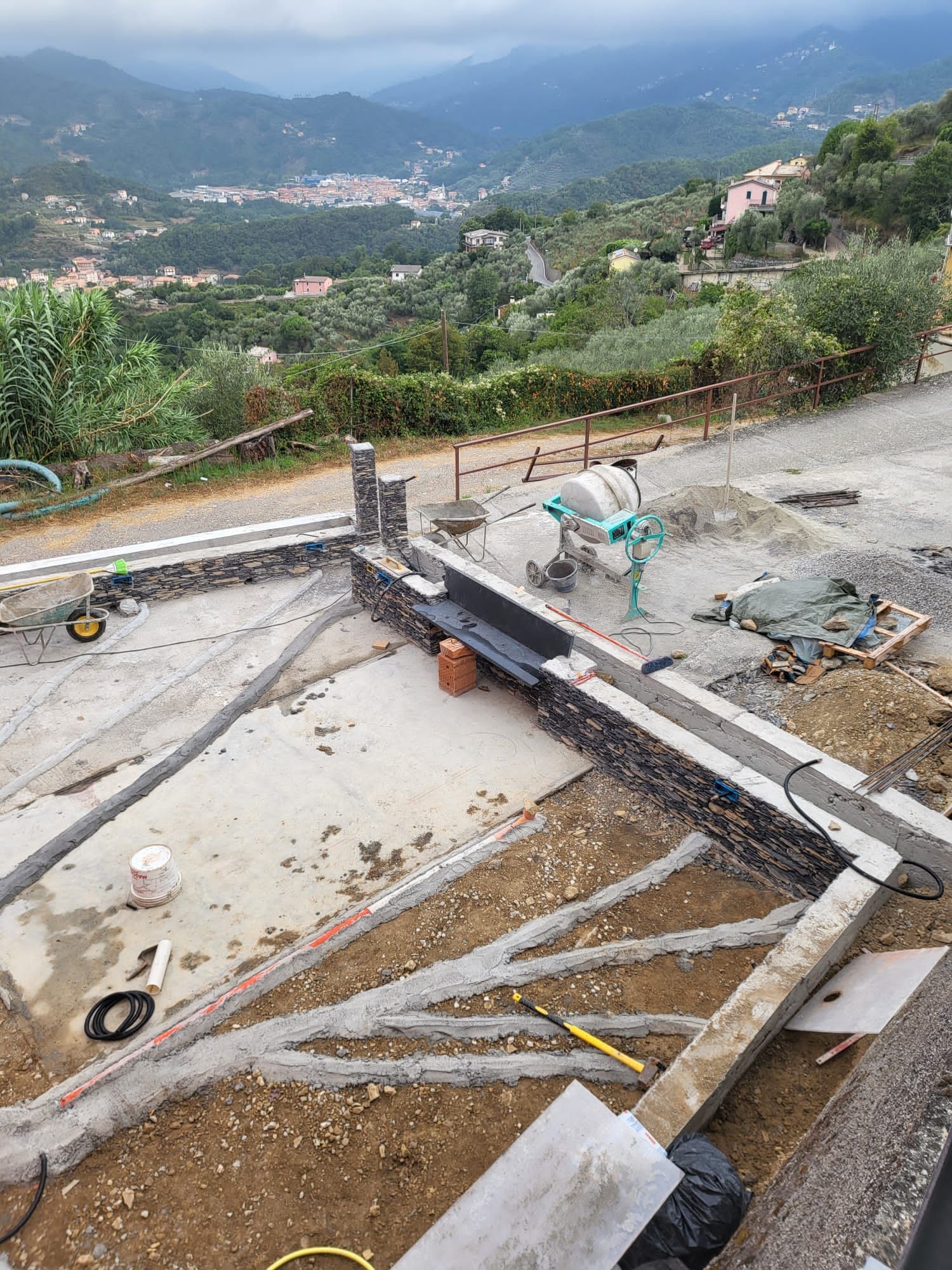 Cantiere con casseforme in cemento, muri di contenimento e vista sulle montagne e su una città.