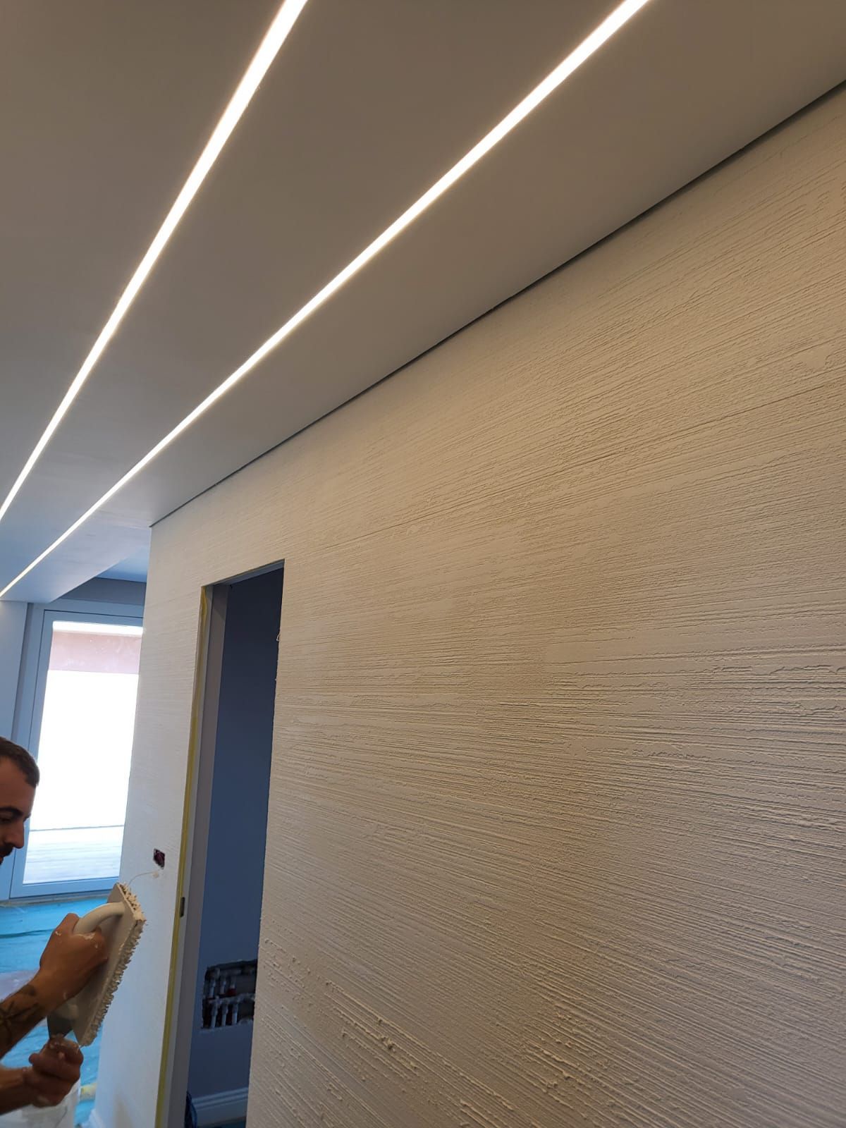 Una persona intonaca una parete di una stanza con luci da incasso nel soffitto.
