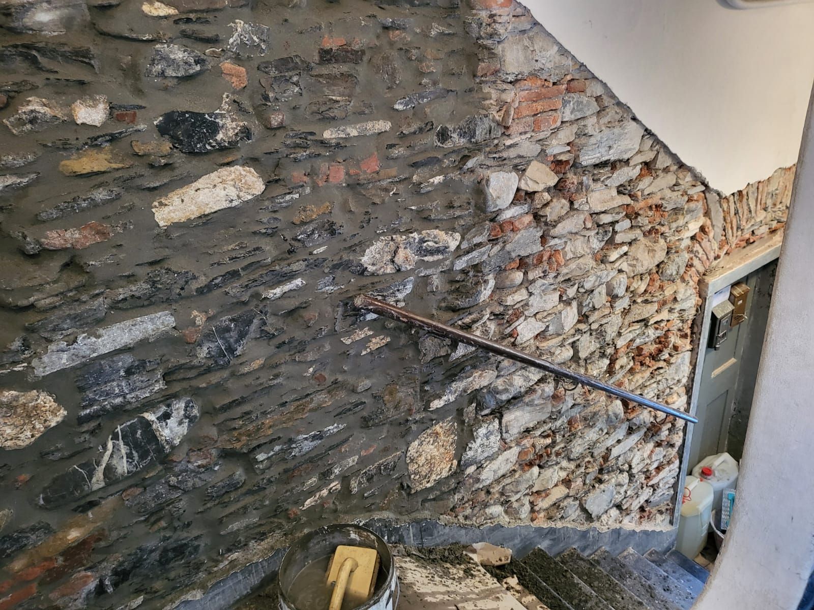 Muro in pietra in fase di ristrutturazione; corrimano; scale; malta; detriti.