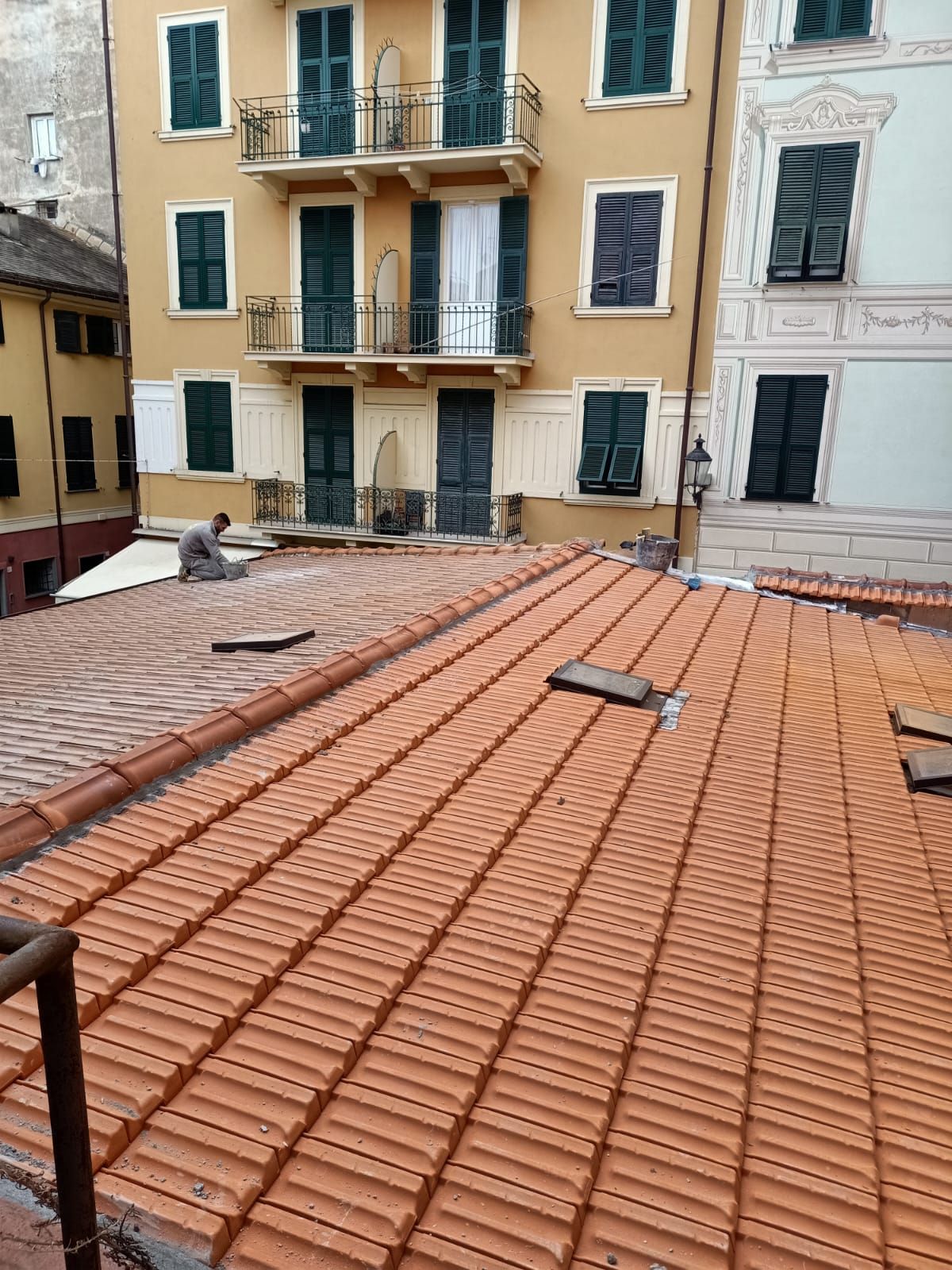 Tetti in terracotta con edifici sullo sfondo. Uomo seduto sul tetto.