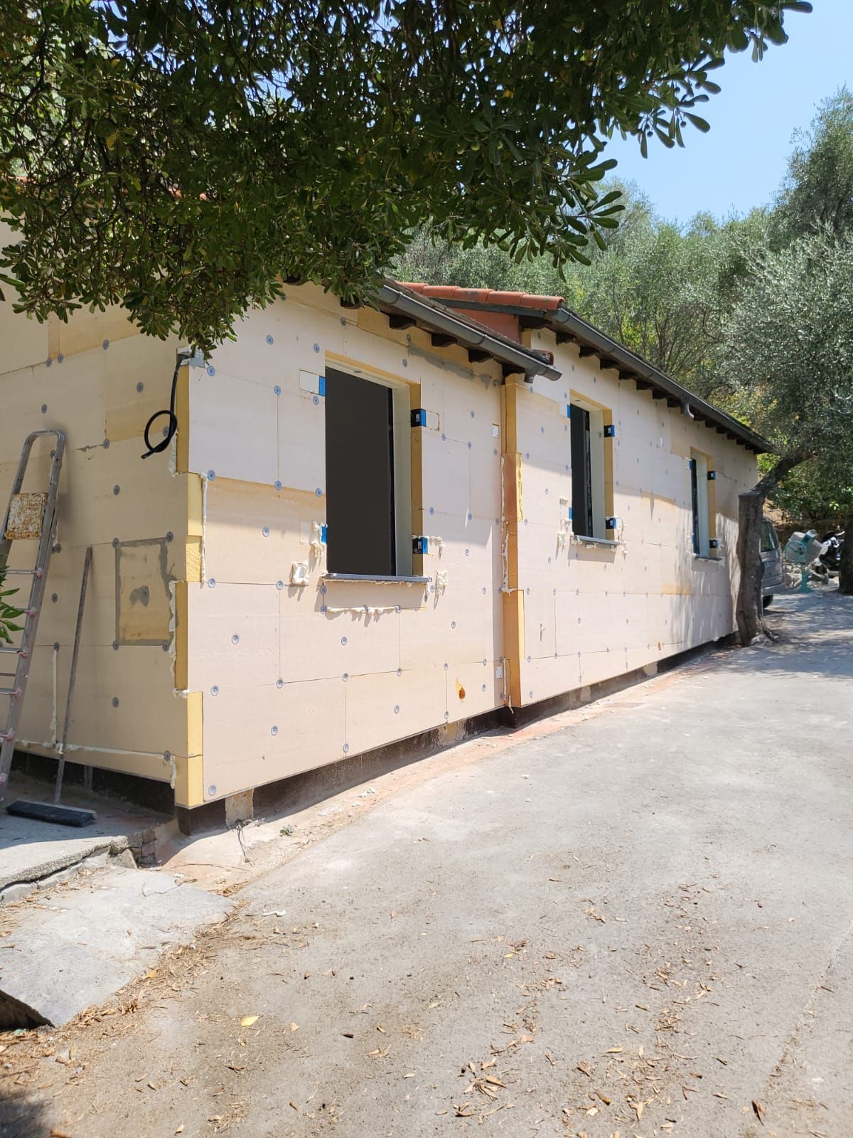 Esterno di un edificio in costruzione, con pannelli isolanti beige e infissi scuri.