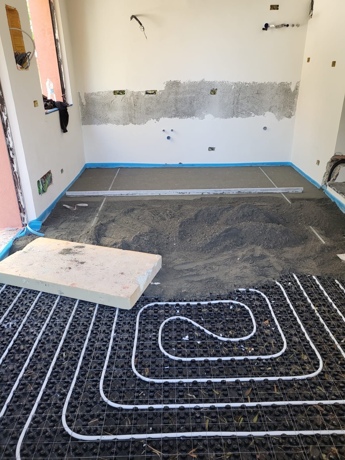 Locale in costruzione con impianto di riscaldamento a pavimento e strato di cemento parzialmente installato.