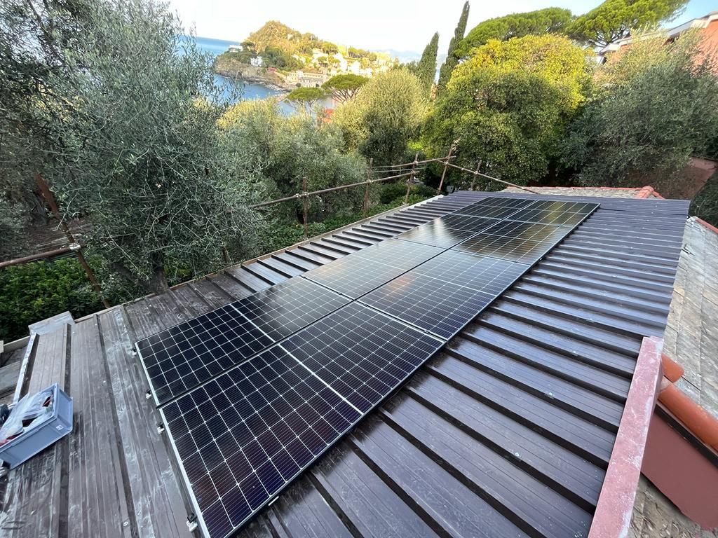 Pannelli solari installati su un tetto di metallo scuro, con vista sulla costa e sugli alberi.