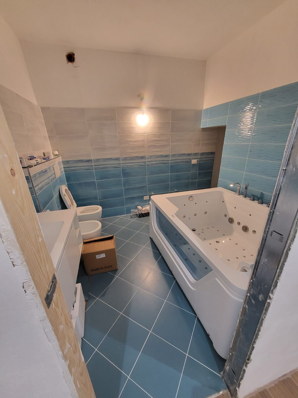 Bagno con piastrelle blu, vasca idromassaggio bianca, WC e lavandino.