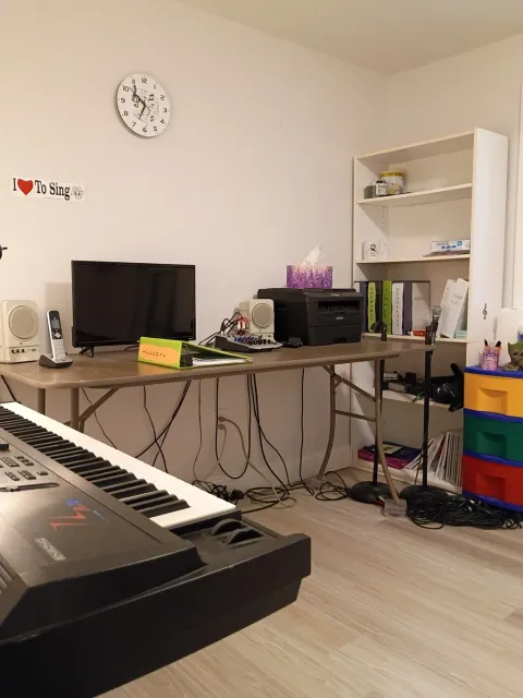 Music teacher demonstrating in a bright studio while a student watches, with guitars and a piano in the background