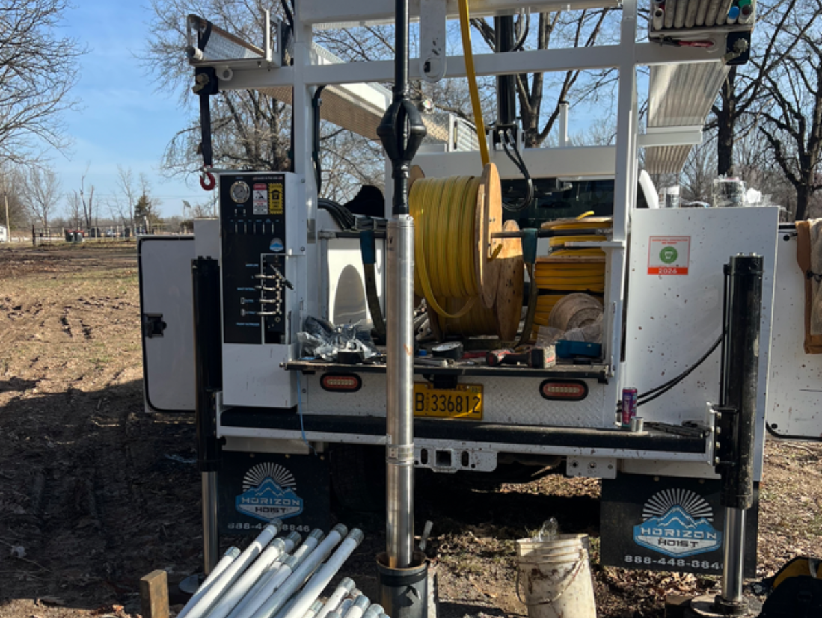 Utility truck with hose reels and pipes parked in a field, viewed from the rear