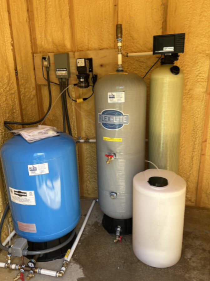 Water softener and filtration system in a utility room with blue, gray, and white tanks.