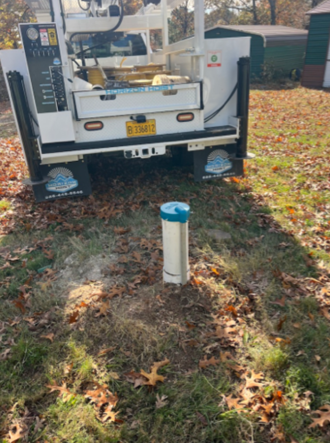 Utility truck parked near a white pipeline vent in a leaf-covered yard