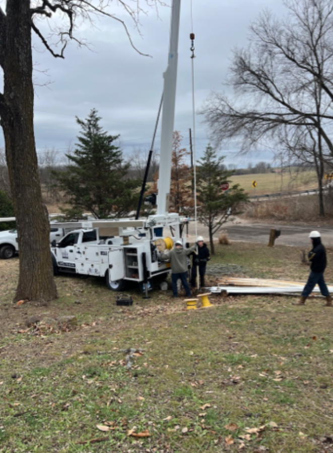 Utility truck and workers beside a raised white crane boom in a grassy park area on an overcast day