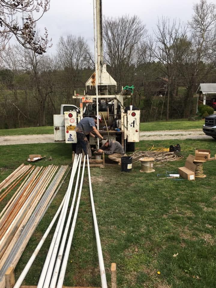 Worker operating a drilling rig beside long metal pipes in a grassy field
