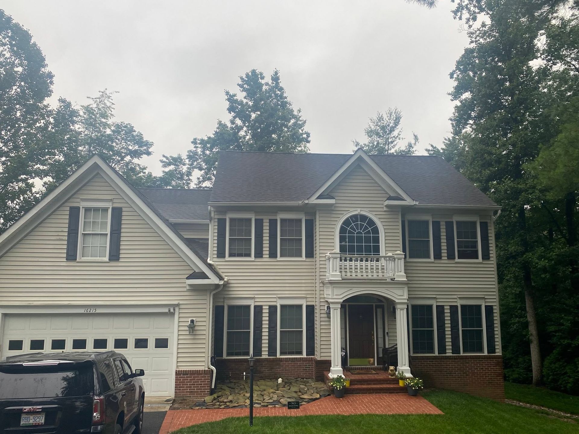 Two-story gray house with white trim, front porch, and attached garage on a tree-lined street.