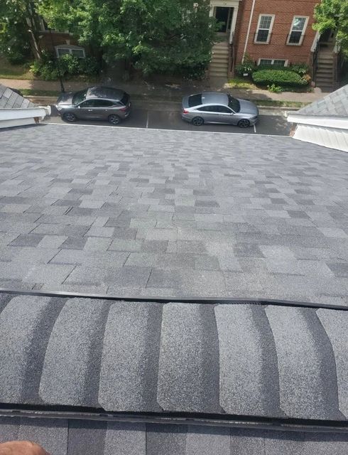 View from a rooftop onto a street with two parked cars, trees, and brick houses across the road