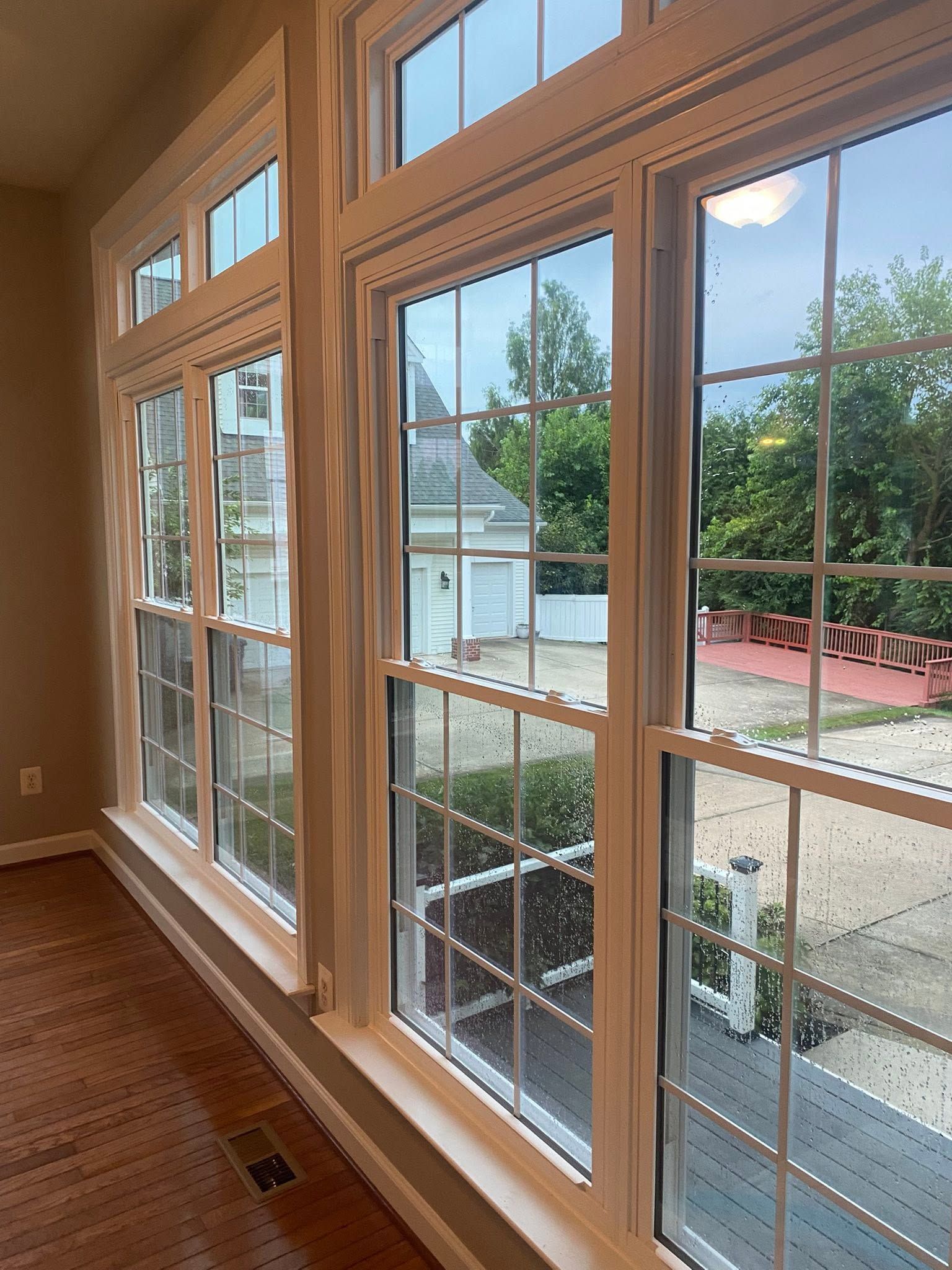 Large windows looking out onto a driveway, trees, and a neighboring house in daylight.