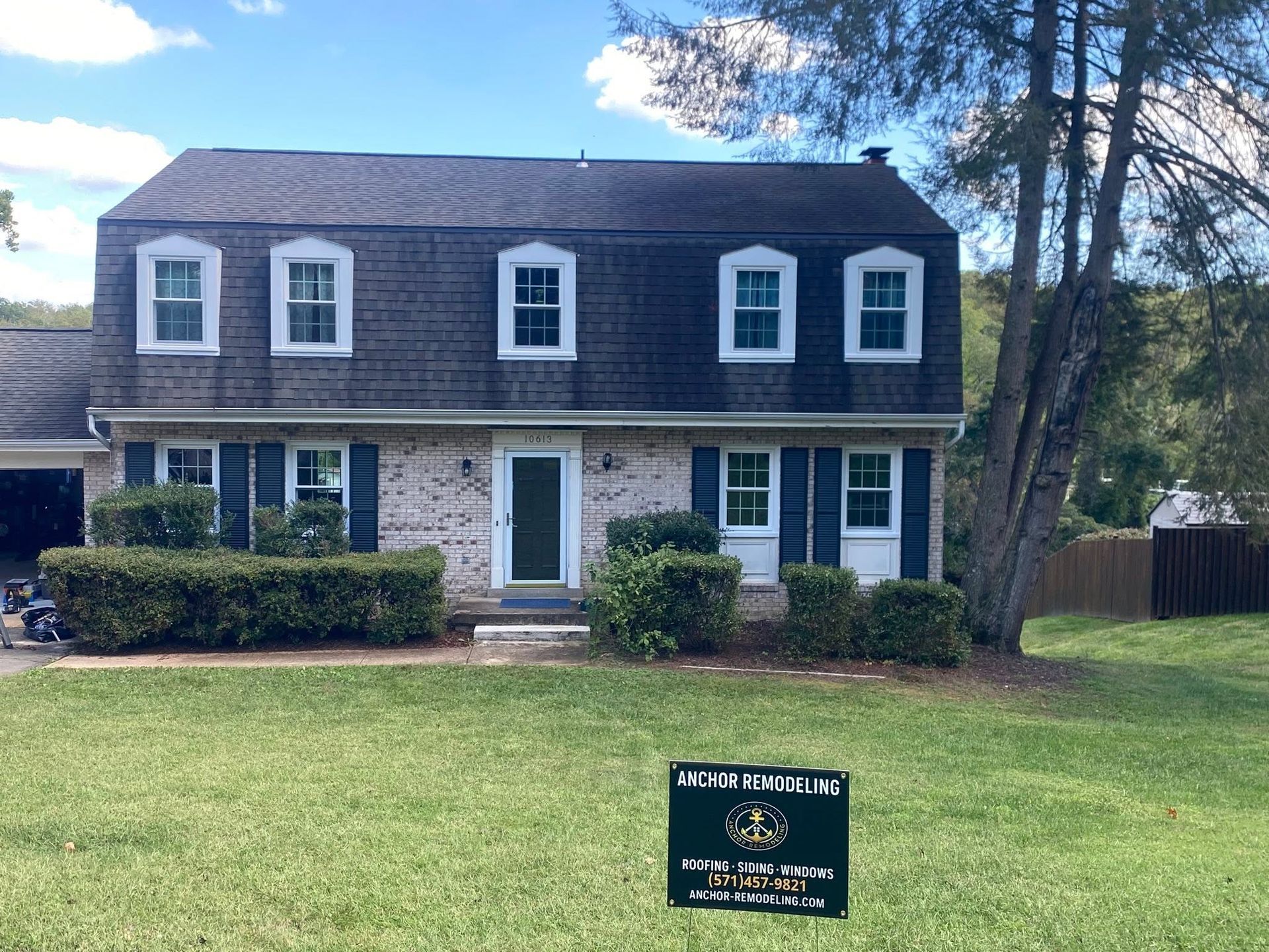 Two-story stone house with dark shingle roof and lawn, seen from the front in daylight