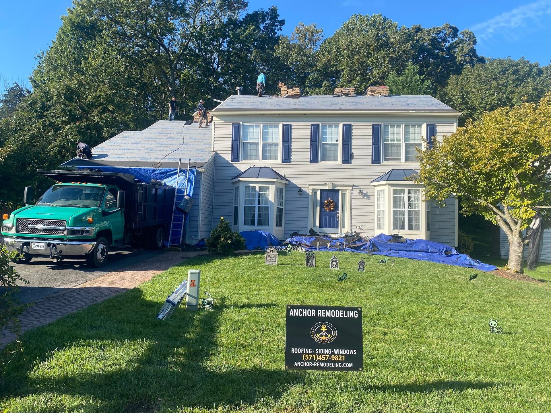 Two-story white house with blue shutters, moving truck in driveway, and lawn sign in front.