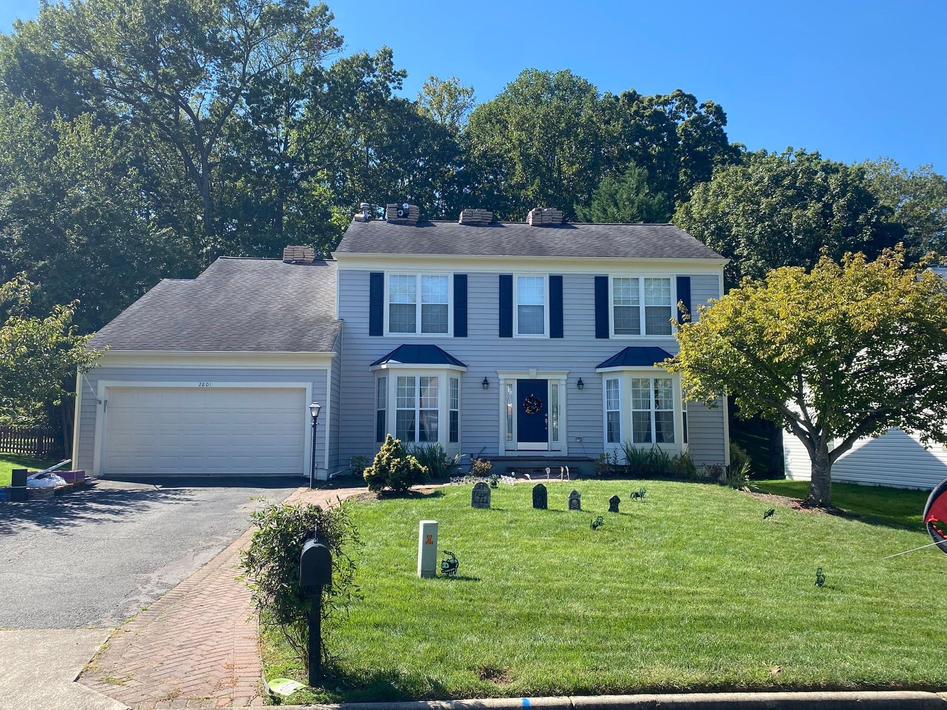 Two-story white suburban house with garage, green lawn, and trees under a clear blue sky