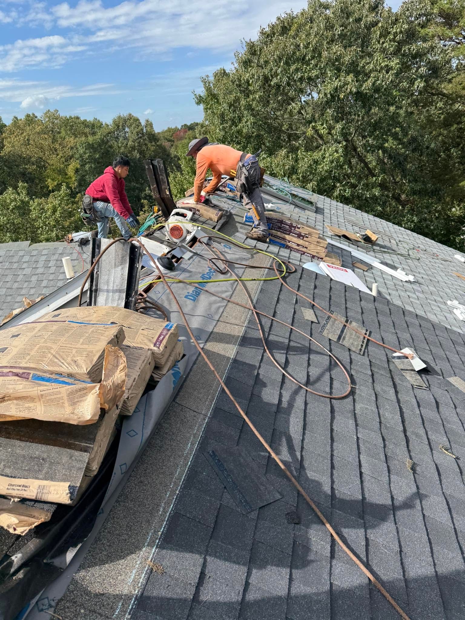 Roofers working on a steep shingled roof with tools and materials nearby