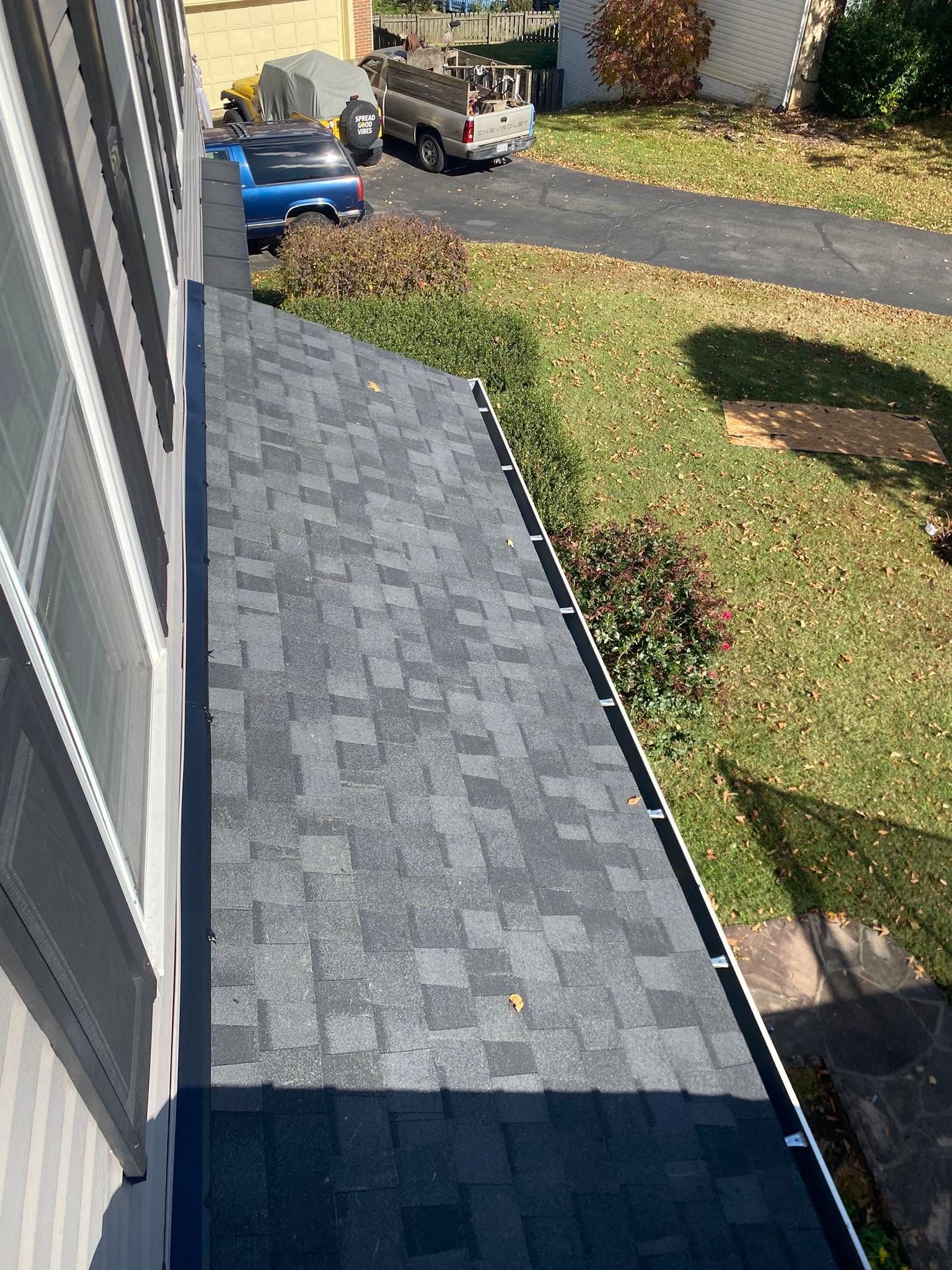 View from a roof edge over a yard, driveway, and parked vehicles on a sunny day