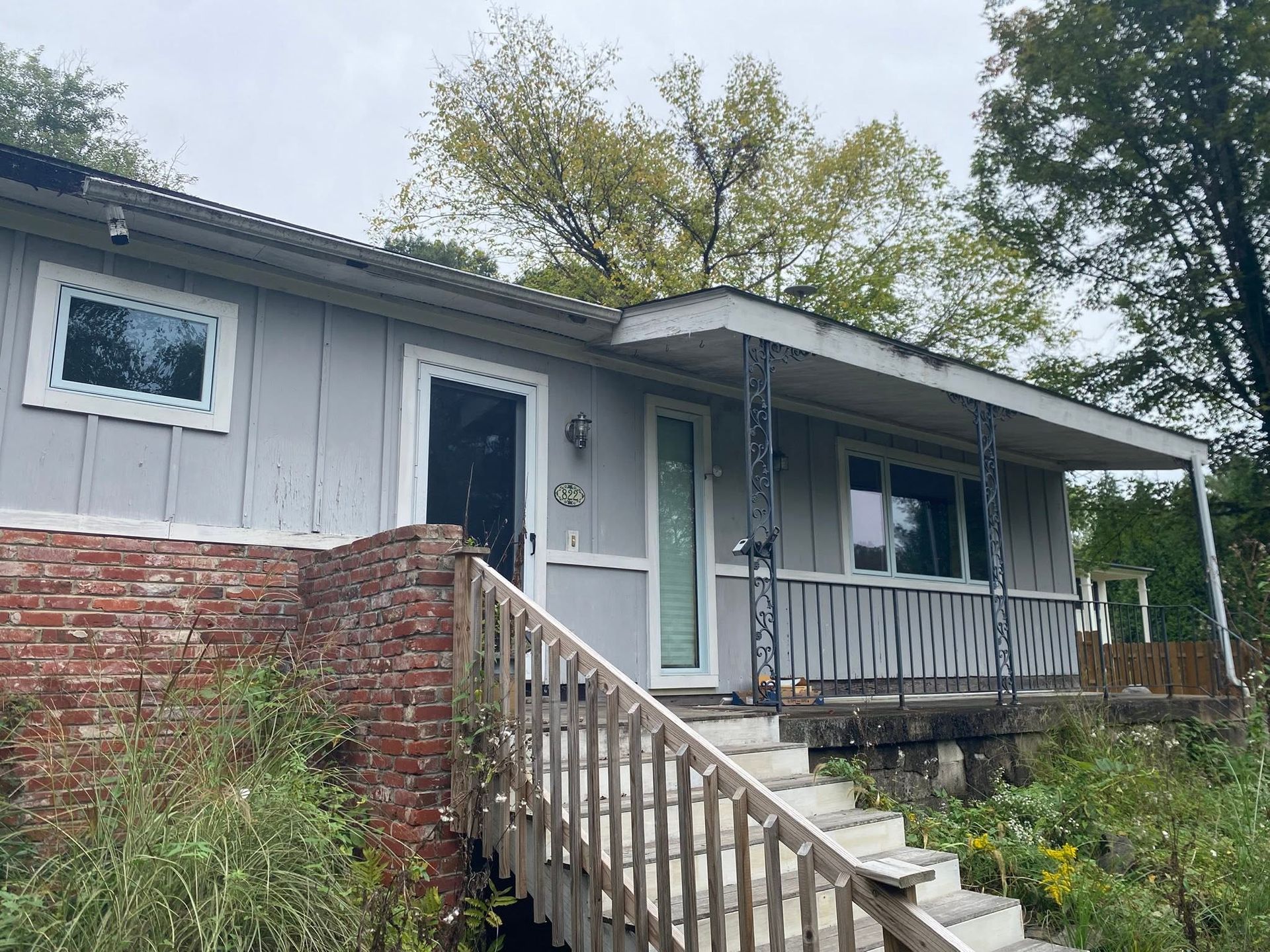 Small gray house with a front porch, railing, and steps leading up from a sloped yard