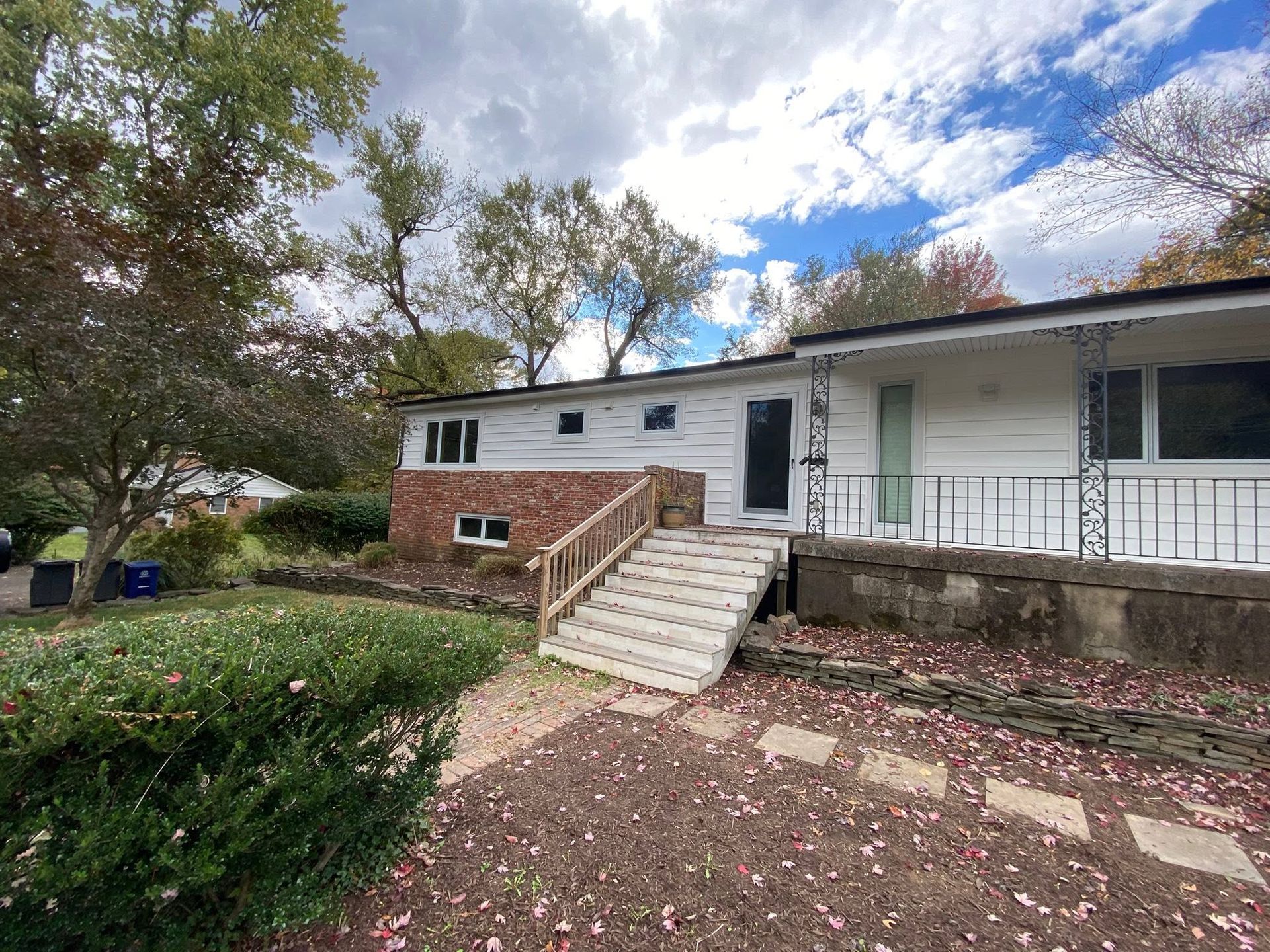 Single-story house with white siding, brick steps, and a front porch surrounded by trees and a leafy yard