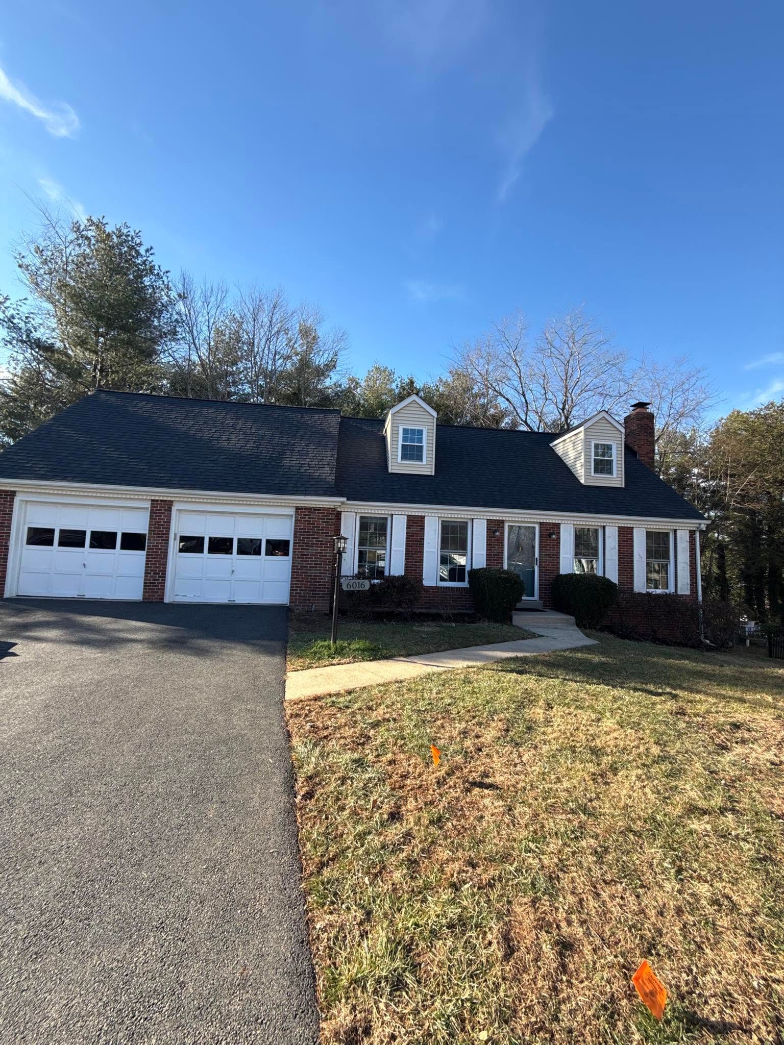 Suburban house with two-car garage, white siding, dark roof, and a front lawn in daylight.