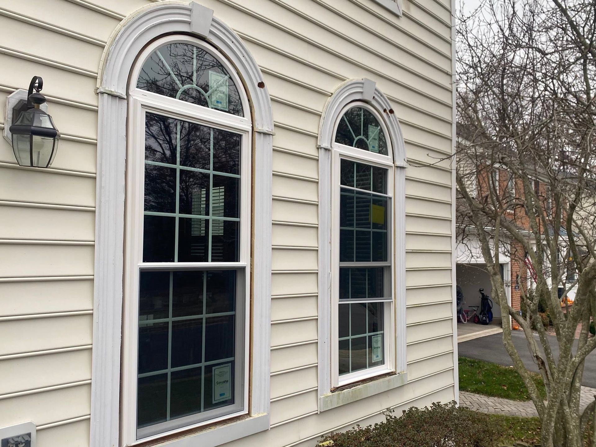 Exterior of a house with two arched windows, beige siding, and a tree in the yard