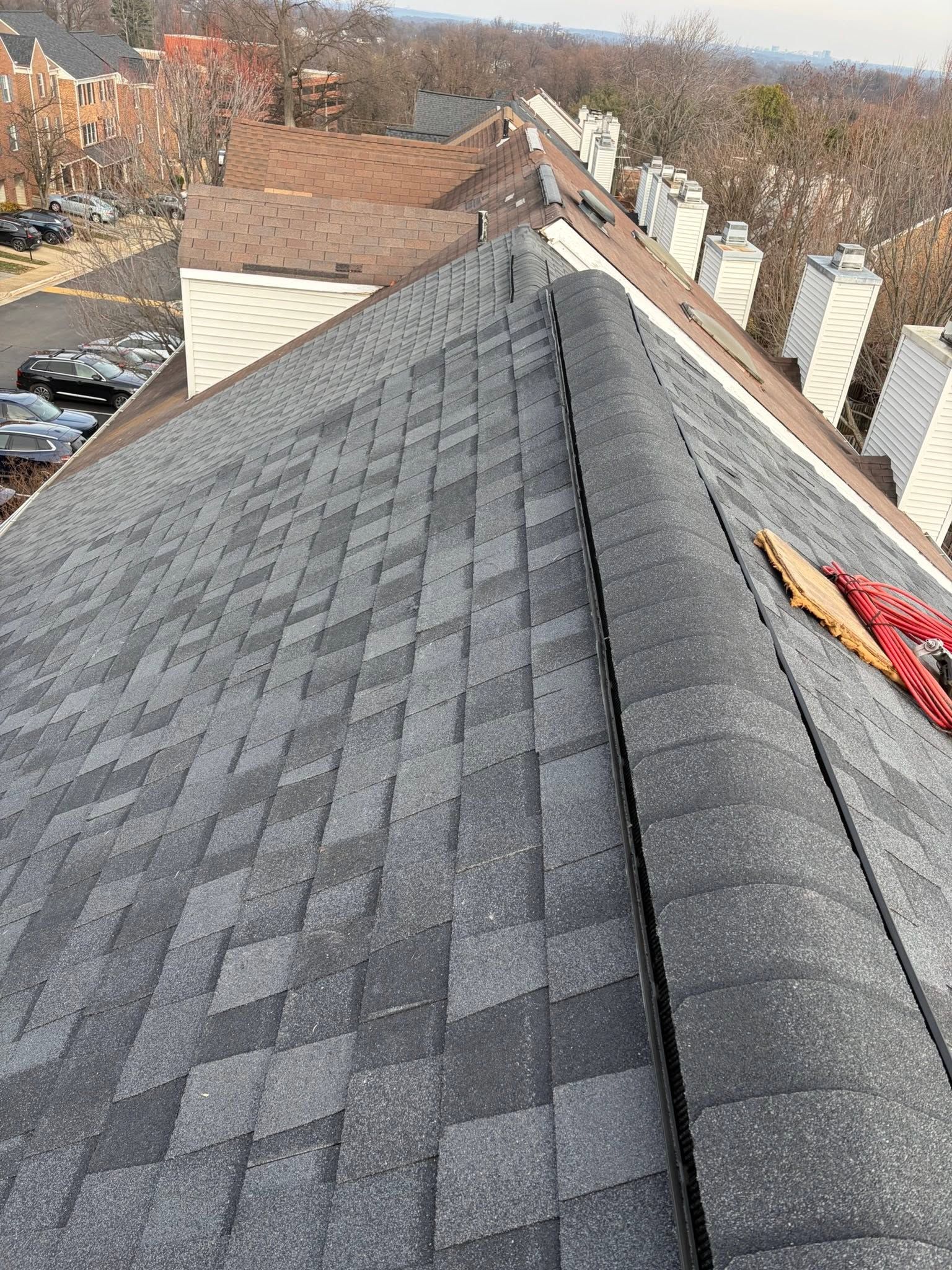 Roof shingles on a house, with a steep roof peak and chimneys in the background