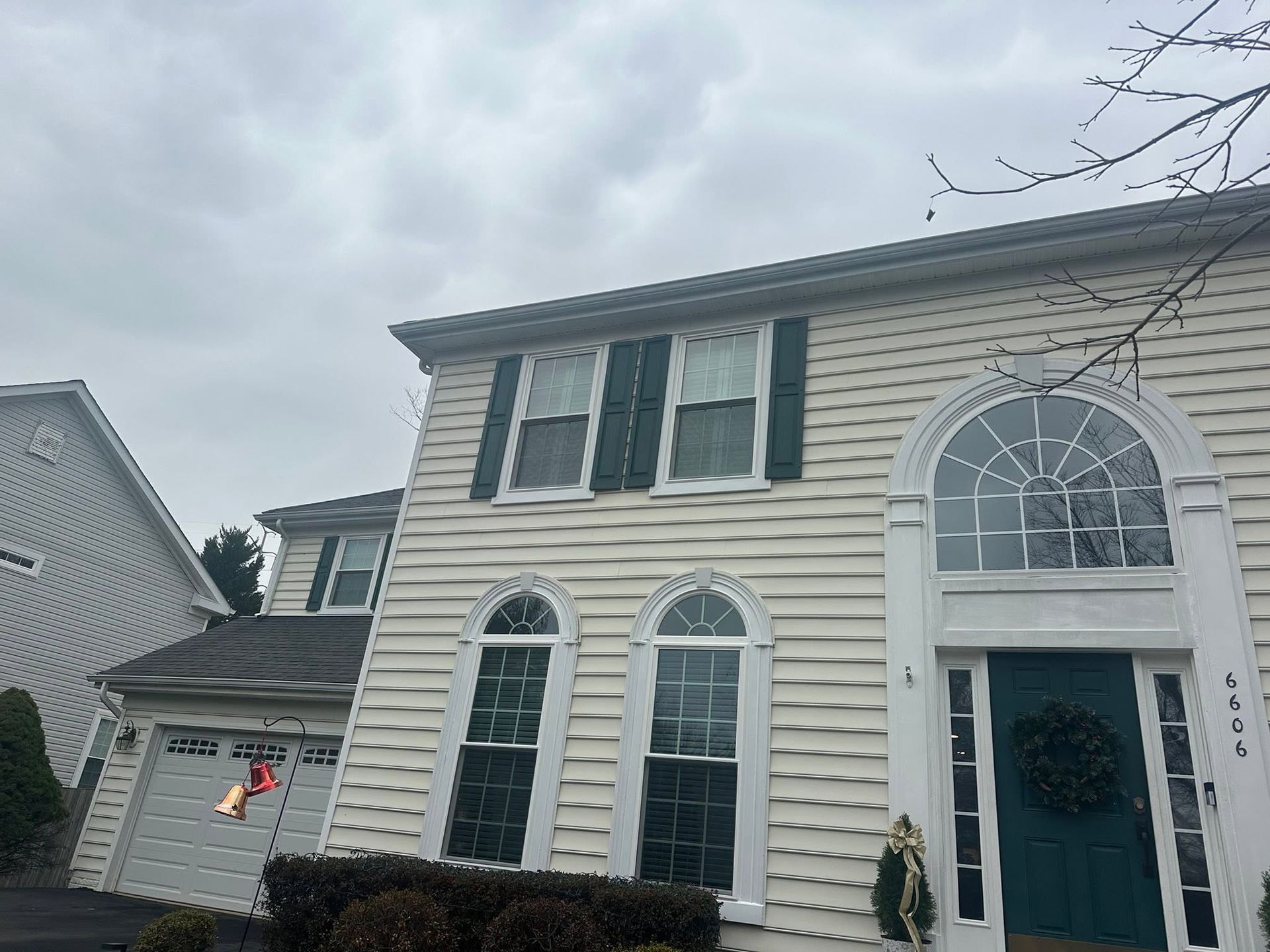 Two-story beige house with arched windows, dark teal front door, and a cloudy sky