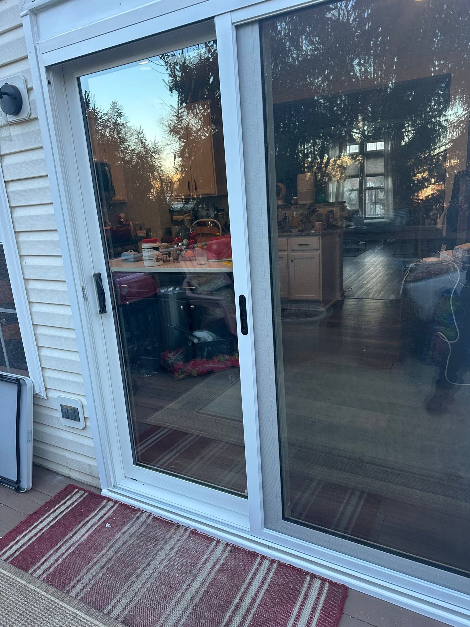Sliding glass door opening to a patio, with striped rug and reflections of outdoor trees.