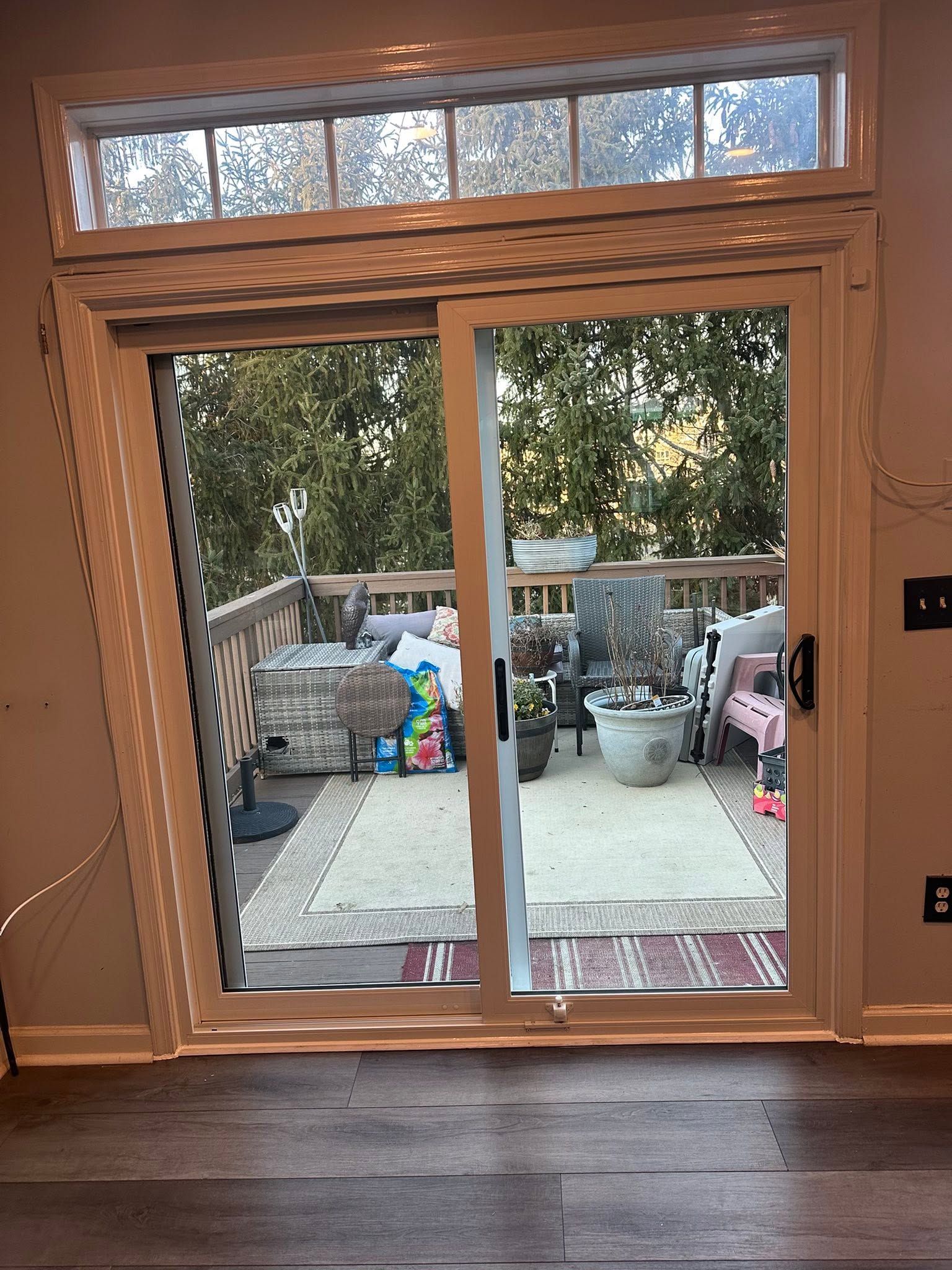 Sliding glass door open to a patio with chairs, bins, and trees outside.