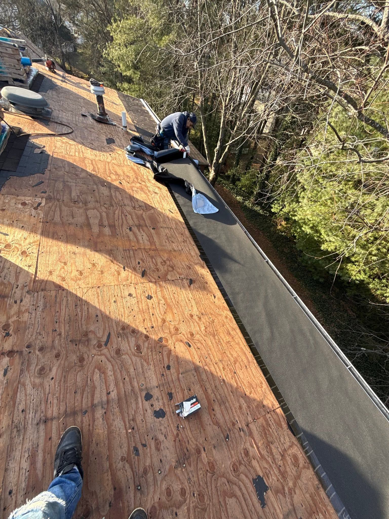 Roofing crew working on a sloped roof, with wood sheathing and trees alongside the house.